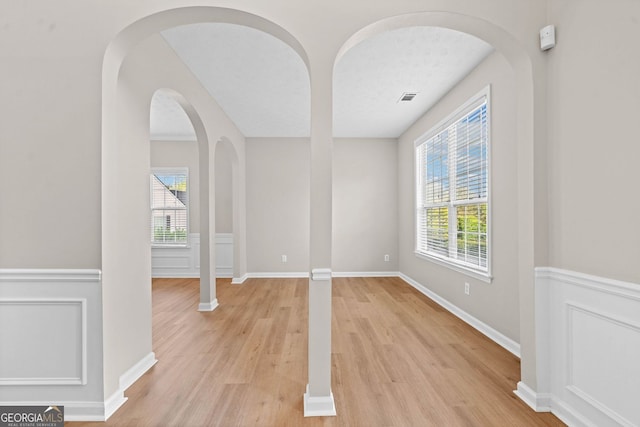 unfurnished dining area with arched walkways, baseboards, visible vents, and light wood-style floors
