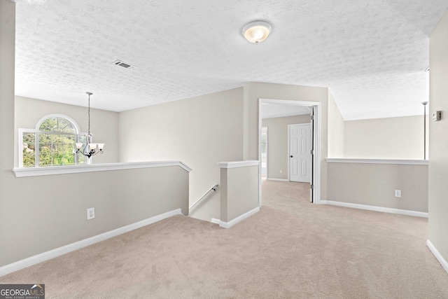 carpeted empty room featuring baseboards, a textured ceiling, a chandelier, and visible vents