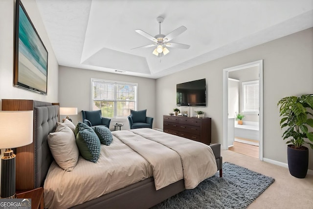 carpeted bedroom with ceiling fan, a raised ceiling, baseboards, ensuite bathroom, and visible vents
