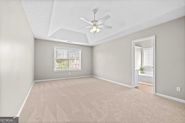 unfurnished bedroom with carpet flooring, a tray ceiling, baseboards, and connected bathroom