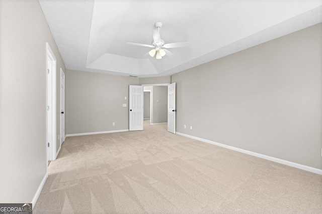 unfurnished bedroom featuring a ceiling fan, baseboards, light colored carpet, and a raised ceiling