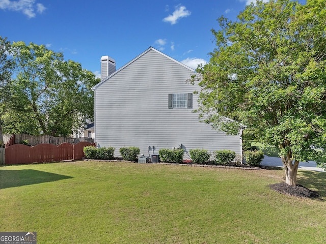 view of side of home featuring fence, a yard, and a chimney