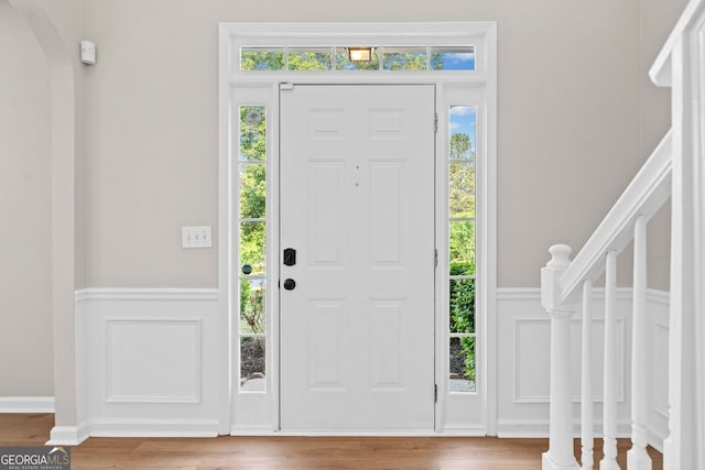 foyer entrance with a wainscoted wall, a decorative wall, arched walkways, and wood finished floors