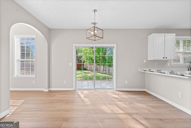 unfurnished dining area with baseboards, a sink, and light wood-style flooring