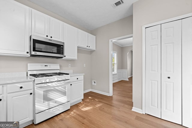 kitchen featuring white gas range oven, light wood finished floors, light countertops, stainless steel microwave, and visible vents