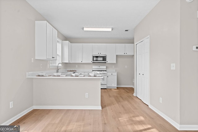 kitchen with light wood-type flooring, light countertops, white gas range oven, stainless steel microwave, and white cabinets
