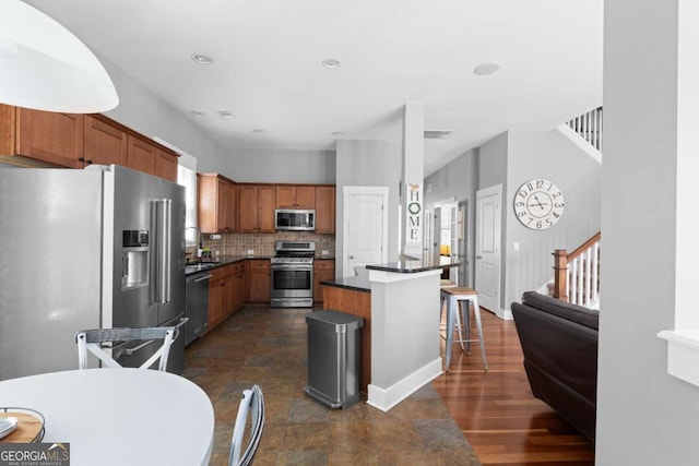 9988 Devonshire St, Douglasville, GA 30135 - kitchen featuring dark countertops, appliances with stainless steel finishes, a breakfast bar, brown cabinetry, and decorative backsplash
