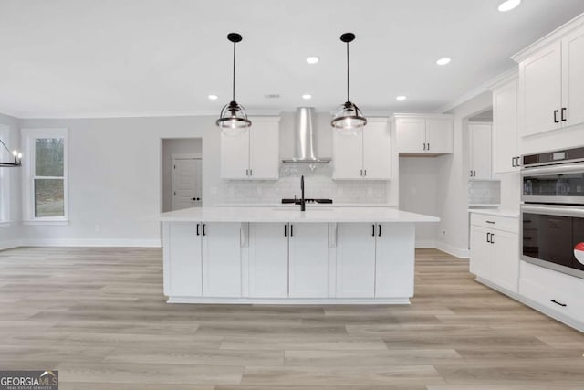 kitchen featuring wall chimney range hood, backsplash, stainless steel double oven, and light countertops