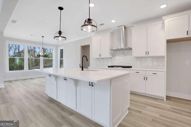 kitchen featuring white cabinets, wall chimney exhaust hood, visible vents, and a sink