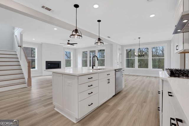kitchen with light wood finished floors, a sink, visible vents, ceiling fan with notable chandelier, and a large fireplace