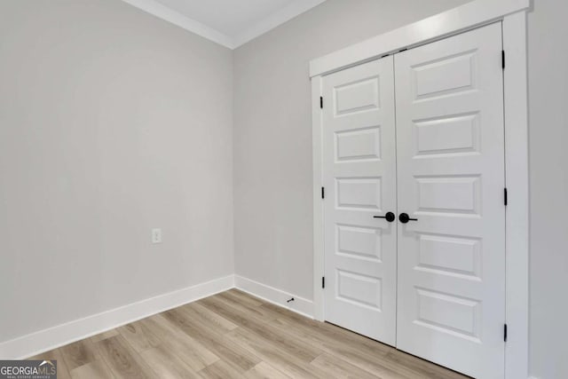 unfurnished bedroom featuring a closet, baseboards, ornamental molding, and light wood-style flooring