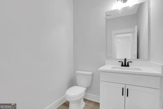 half bathroom featuring baseboards, wood finished floors, vanity, and toilet