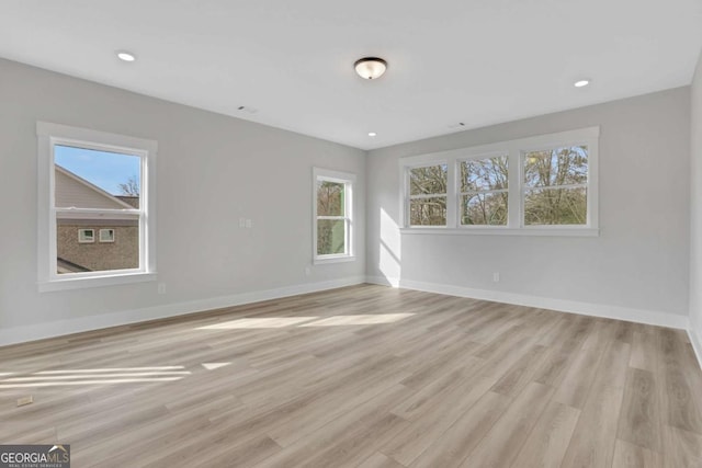 spare room with recessed lighting, plenty of natural light, baseboards, and light wood-style flooring