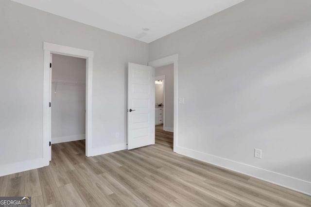 unfurnished bedroom featuring light wood finished floors, baseboards, a spacious closet, and a closet