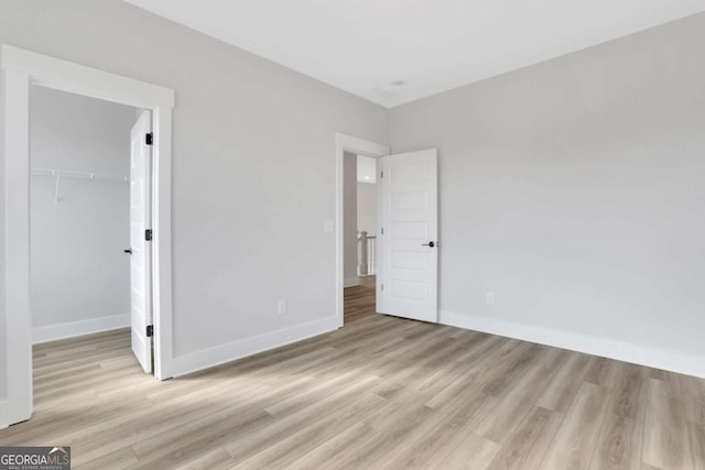unfurnished bedroom featuring light wood-style flooring, baseboards, a closet, and a walk in closet