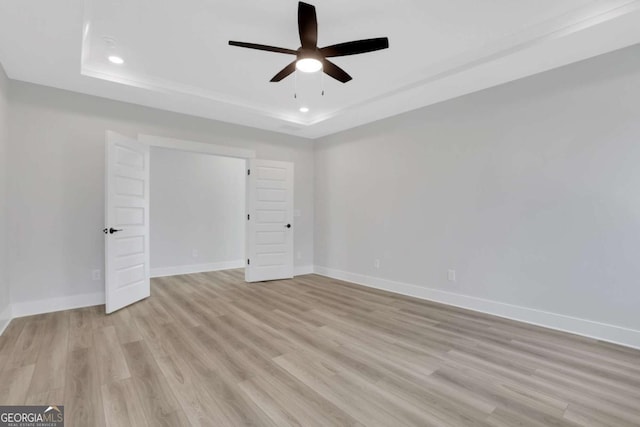spare room with a raised ceiling, light wood-style flooring, baseboards, and ceiling fan