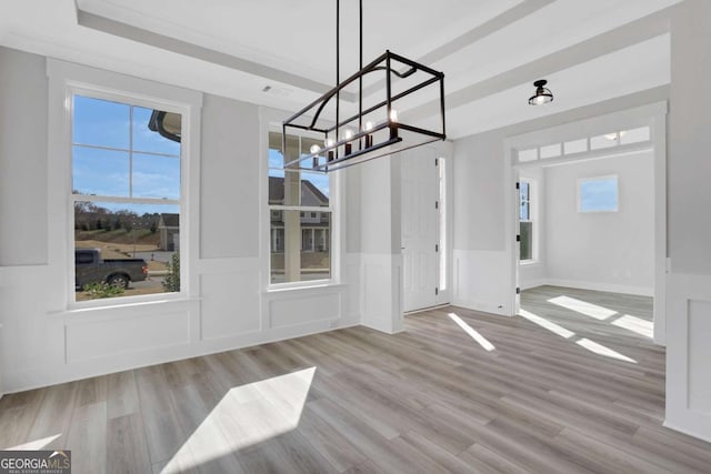 unfurnished dining area with wood finished floors, a decorative wall, and a notable chandelier
