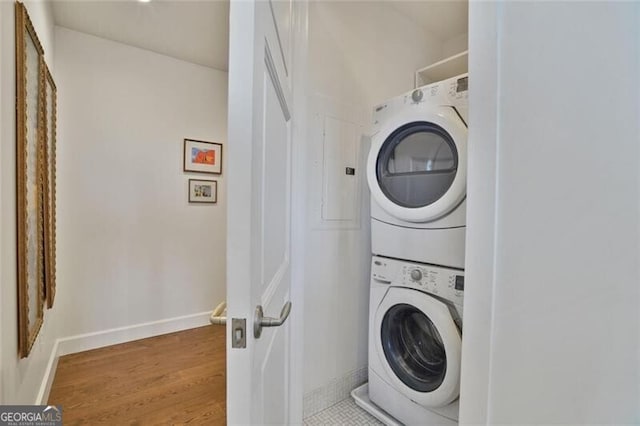 laundry room featuring laundry area, stacked washer and dryer, baseboards, and wood finished floors