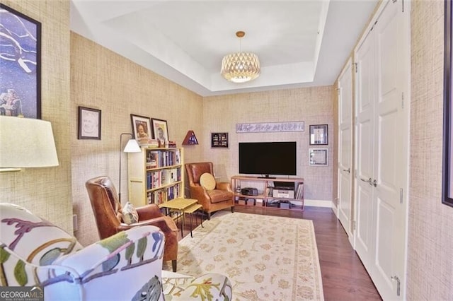 sitting room with a tray ceiling, an inviting chandelier, and dark wood finished floors