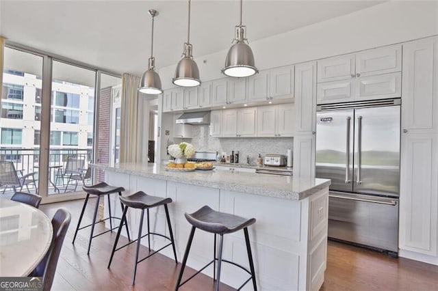 kitchen with stainless steel built in refrigerator, light stone counters, dark wood finished floors, under cabinet range hood, and white cabinets