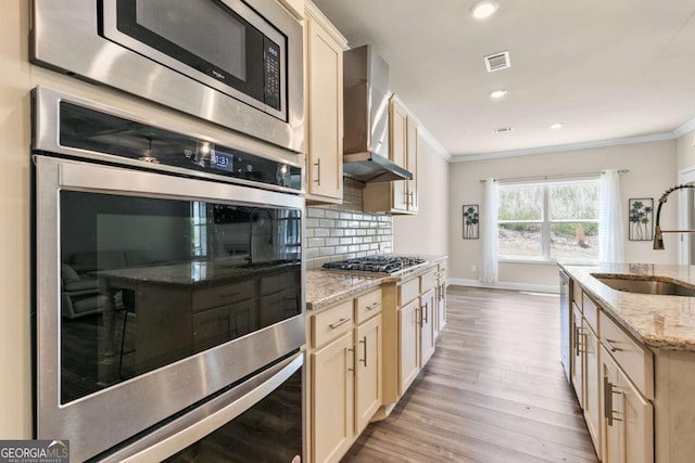 kitchen with wall chimney exhaust hood, appliances with stainless steel finishes, ornamental molding, and a sink