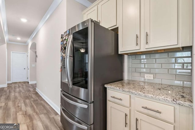 kitchen with arched walkways, stainless steel fridge, light wood-style floors, decorative backsplash, and ornamental molding