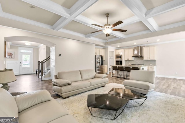 living area with a ceiling fan, light wood-style floors, arched walkways, beamed ceiling, and coffered ceiling