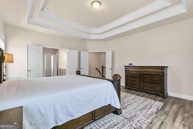 bedroom with baseboards, wood finished floors, a raised ceiling, and crown molding