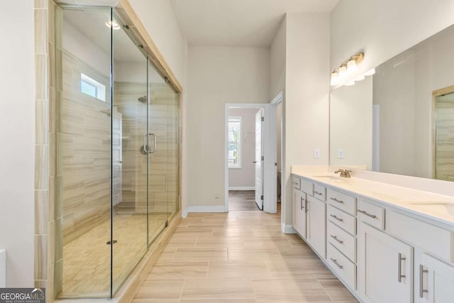 full bath featuring baseboards, double vanity, plenty of natural light, and a stall shower