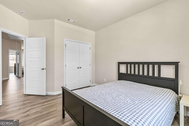 bedroom featuring baseboards, visible vents, light wood finished floors, and a closet