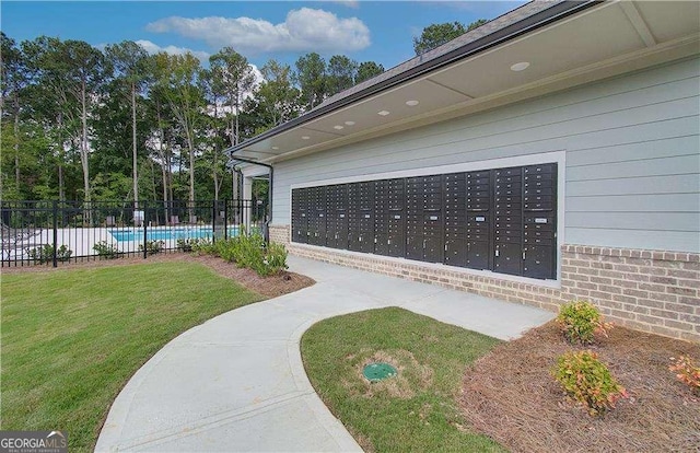 view of property's community featuring mail area, a lawn, and fence
