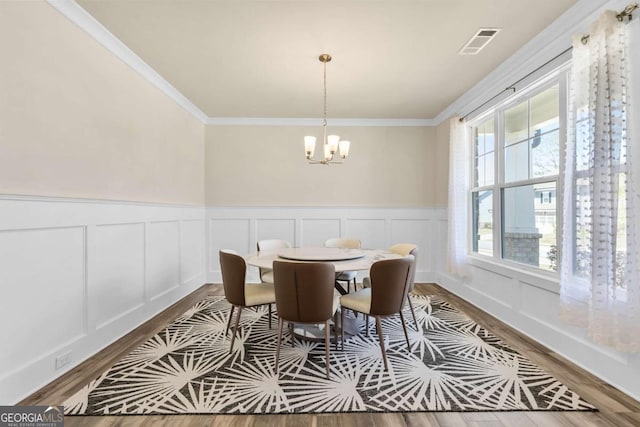 dining room featuring an inviting chandelier, wood finished floors, visible vents, ornamental molding, and wainscoting