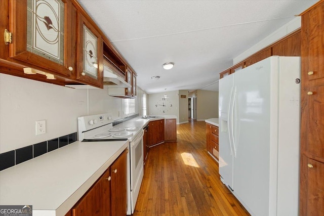 kitchen with brown cabinetry, wood-type flooring, and white appliances