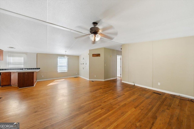 unfurnished living room with lofted ceiling, wood finished floors, visible vents, baseboards, and ceiling fan
