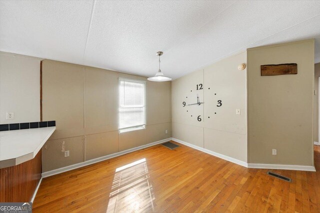 unfurnished dining area featuring light wood finished floors, baseboards, visible vents, and a textured ceiling