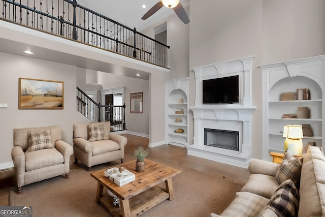 living room with a towering ceiling, wood finished floors, baseboards, ceiling fan, and stairway