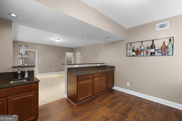 kitchen featuring baseboards, a sink, dark stone countertops, and a peninsula