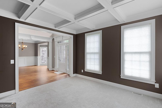 carpeted empty room with a notable chandelier, beam ceiling, visible vents, and coffered ceiling