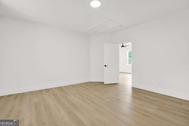 spare room featuring attic access, baseboards, and wood finished floors