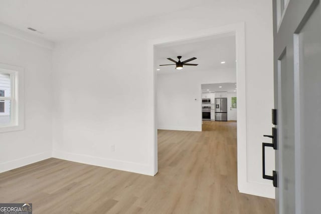 spare room with light wood-type flooring, a ceiling fan, baseboards, and a wealth of natural light