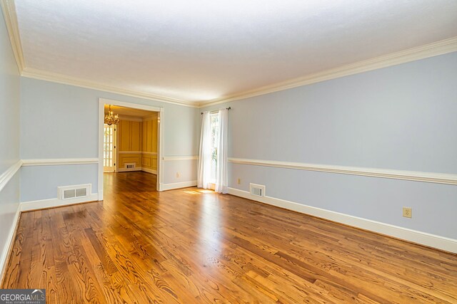 spare room with a chandelier, crown molding, wood finished floors, and baseboards