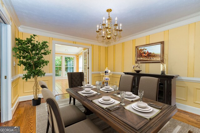 dining space featuring a decorative wall, a chandelier, crown molding, wood finished floors, and wainscoting