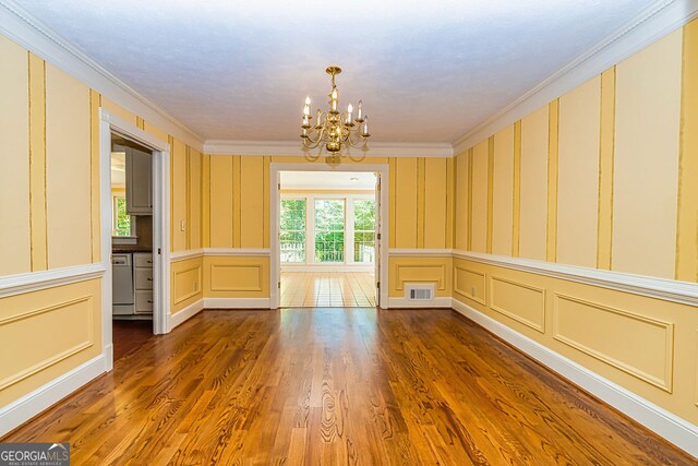spare room featuring a decorative wall, a chandelier, crown molding, dark wood-style flooring, and wallpapered walls