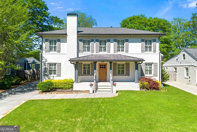 colonial-style house featuring a chimney, a porch, a standing seam roof, and brick siding
