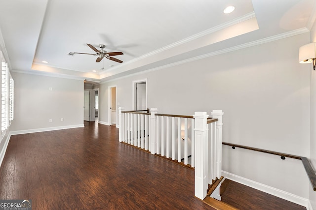 unfurnished room featuring a tray ceiling, wood finished floors, a ceiling fan, baseboards, and crown molding