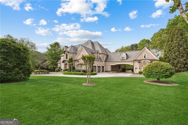 view of front of property featuring a front yard, a chimney, curved driveway, and stone siding