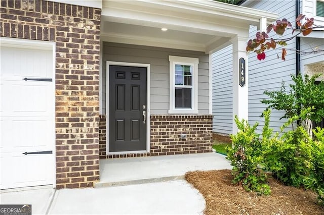 view of exterior entry with brick siding, a garage, and covered porch