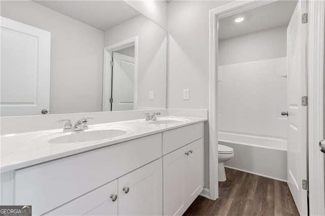 full bath with wood finished floors, a sink, double vanity, and toilet