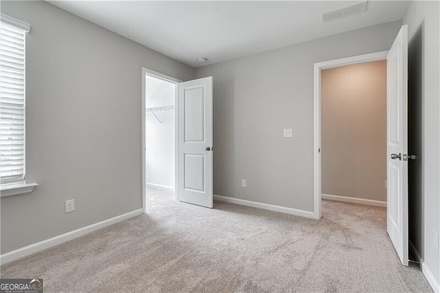 unfurnished bedroom with a closet, a spacious closet, carpet floors, baseboards, and visible vents