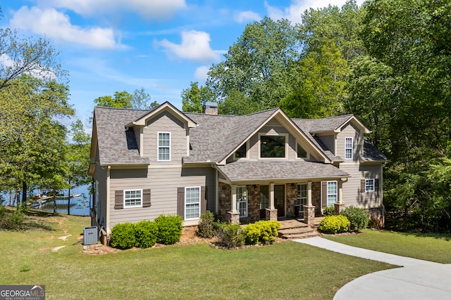craftsman inspired home with central air condition unit, a chimney, a shingled roof, a porch, and a front yard